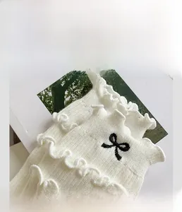 Detail of white cotton socks featuring ruffled cuffs and a delicate black embroidered bow