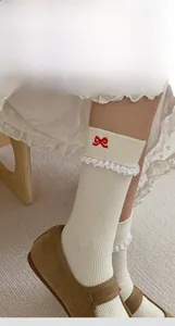 Close-up of white ribbed crew socks with delicate lace trim and red bow embroidery