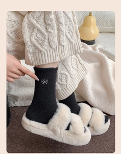 Detail of black thermal socks with white camellia embroidery worn with plush slippers