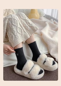 Detail of plush faux fur slippers with floral embroidered black knit thermal socks