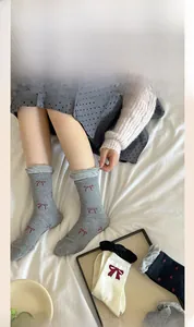 Detail of grey crew socks with red bow pattern and knitted cotton texture on white bedding