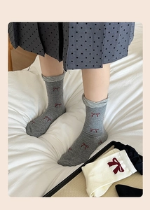 Detailed view of grey and cream cotton socks featuring red bows in a cozy home setting