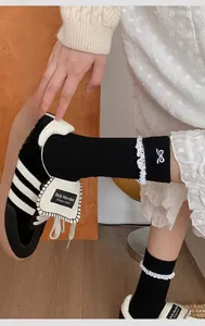 Close-up of black crew socks with white lace trim and bow embroidery details