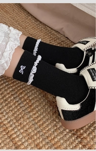 Close-up of black ribbed mid-calf socks with white lace trim and bow embroidery details