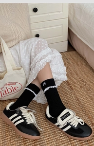Detail of black mid-calf cotton socks featuring white lace trim and delicate bow accent