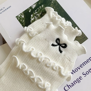 Beige cotton socks with embroidered bow and ruffled edges on vintage magazine