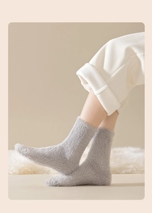 Close-up of thick plush mink velvet socks in light grey on a soft white carpet background