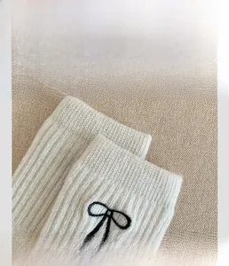 Detailed close-up of white ribbed wool socks featuring an embroidered black bow detail