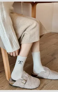 Detail of wool socks with bow embroidery shown with cozy slippers on a wooden floor
