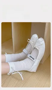 Dettaglio ballerine Tabi bianche con fiocco e calze a rete su pavimento in legno chiaro