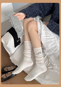 Close-up of white calf socks with black bow embroidery and vertical ribbed texture