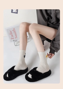 Detail of cream flecked cotton socks with cute cat embroidery and black plush slippers