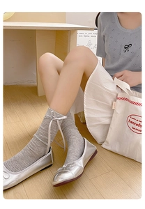 Dettaglio calze grigie a costine con fiocchi di raso bianchi e scarpe ballerine