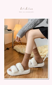 Detail of white plush slippers with knit socks featuring a delicate bow embroidery