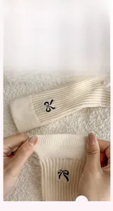 Detail of beige knit sock showing elastic ribbed cuff with black bow embroidery