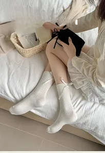 Close-up of white ribbed cotton mid-calf socks with delicate satin bow details