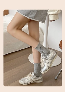 Detailed view of silver metallic sneakers with grey cotton socks featuring safety pin embroidery