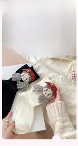 Detail of knitted socks featuring a 3D cartoon girl doll with red crochet hat and tassels