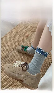 Detail of grey crew socks with blue ruffle trim paired with brown suede sneakers