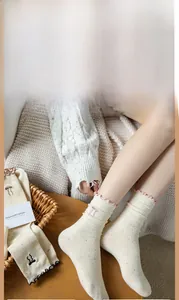 Detail of beige speckled mid-calf socks with pink ruffled cuffs and bow embroidery