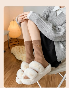 Detail view of brown ribbed cotton socks with bow embroidery and white plush slippers