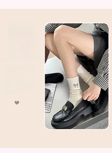 Detail of cream white ribbed socks featuring a delicate silver-grey bow and black loafers