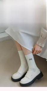 Detail of white rib-knit socks featuring delicate black embroidered bows with loafers