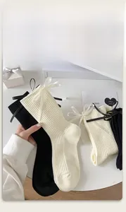 Close-up of white and black ribbed cotton socks featuring elegant silk ribbon bow details