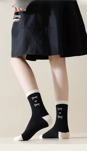 Close-up of black cotton mid-calf socks with white bow heart patterns and speckle yarn