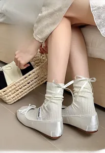 Detail of white ribbed crew socks with silky bow paired with ballet flats on a model