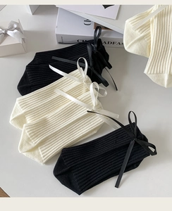 Detail of knit ribbed mid-calf socks with silky bow accents in black and cream
