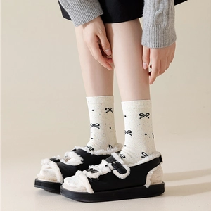 Bow pattern cotton crew socks worn with platform fuzzy sandals in a studio setting