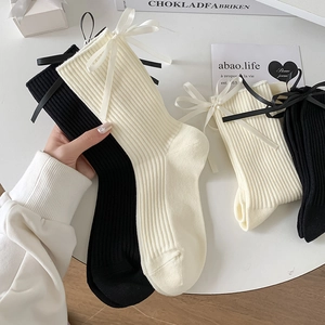 White and black cotton crew socks with satin bow accents in a stylish lifestyle display