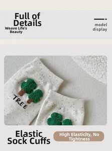 Close-up of elastic ribbed cuff on white knit socks featuring green tree embroidery