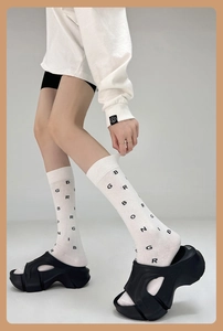 Detail of white cotton mid-calf socks with black letter print worn with platform sandals