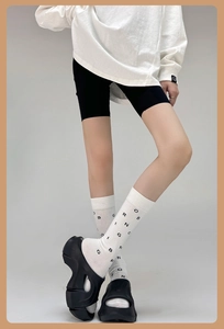 Close-up of white calf socks with black letter print and smiley detail on a model