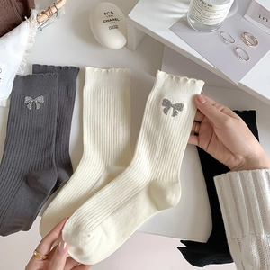 Knit mid-calf socks with silver bow accents and ruffled edges in neutral colors