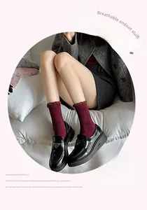 Detailed view of burgundy crew socks with bow jacquard pattern and black leather loafers