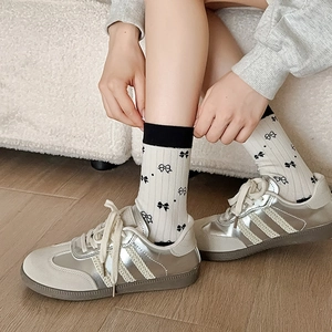 White cotton crew socks with black bow patterns and vintage sneakers on wooden floor