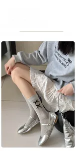 Detail of light gray crew socks with black cross embroidery and silver Mary Jane shoes