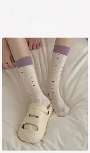 Detail of cream crew socks with purple ribbed cuffs and colorful heart jacquard patterns