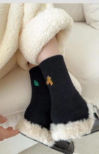 Detail of a thick black winter sock with embroidered giraffe and leaf patterns
