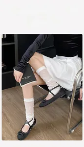 Close-up of white mesh leg warmers paired with lace-up ballet flats on wooden floor