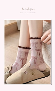Detail of pink cotton socks featuring brown bow jacquard and ruffled edges on wooden floor