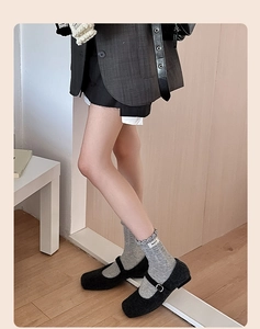 Detail of light grey knit socks with ruffled cuffs and black Mary Jane shoes on wood floor