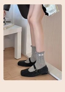 Close-up of light grey ruffle socks paired with charcoal mary jane shoes and brand tag
