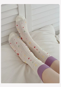 Detail view of cream socks featuring colorful heart patterns and purple ribbed cuffs