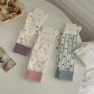 Three pairs of white cotton socks with heart and floral patterns in a cozy setting