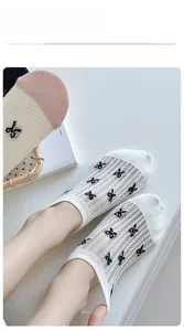 Detail of white mesh socks featuring black bow pattern and pink heel detail on a white surface