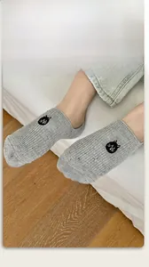 Close-up of light grey no-show sock with cartoon cat embroidery and speckled knit texture